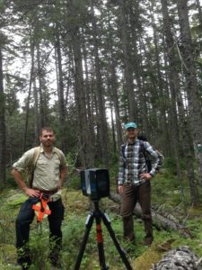 Two men stand in the woods with the scanner equipment between them.