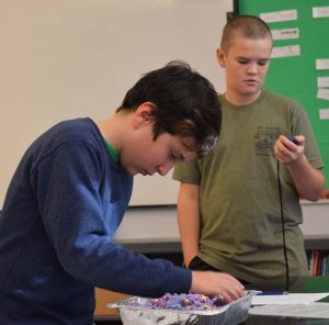 a student sifts through colored materials in a foil pan while another watches a timer