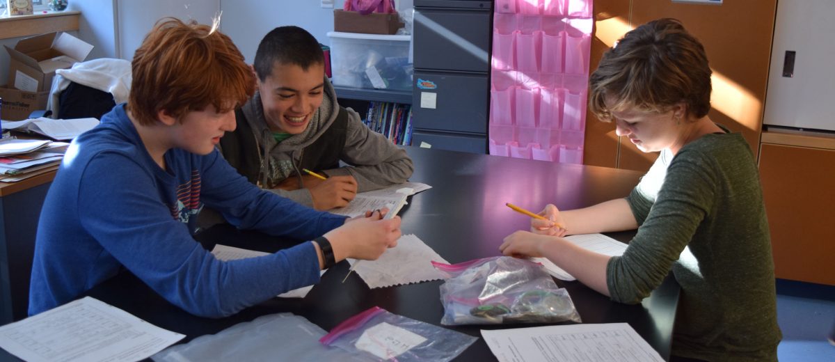 three students examine materials on a table