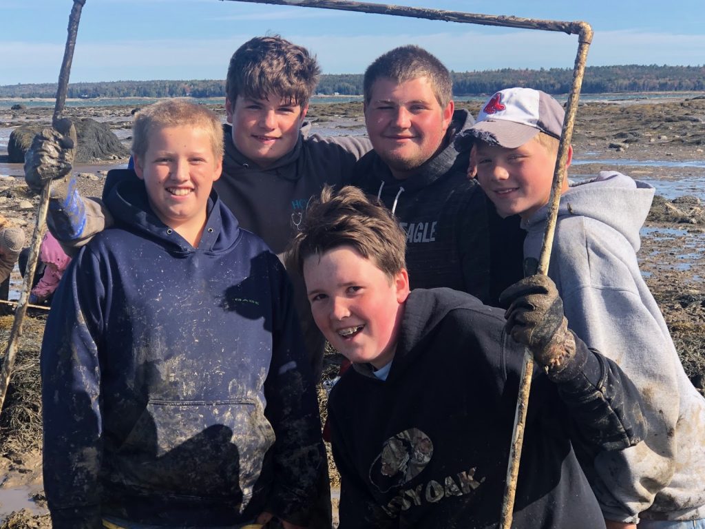 Five smiling muddy students holding a quadrat frame