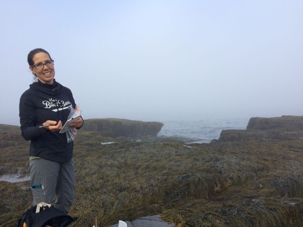 Hannah Webber smiling from the rockweed-covered rocks in the low-tide zone