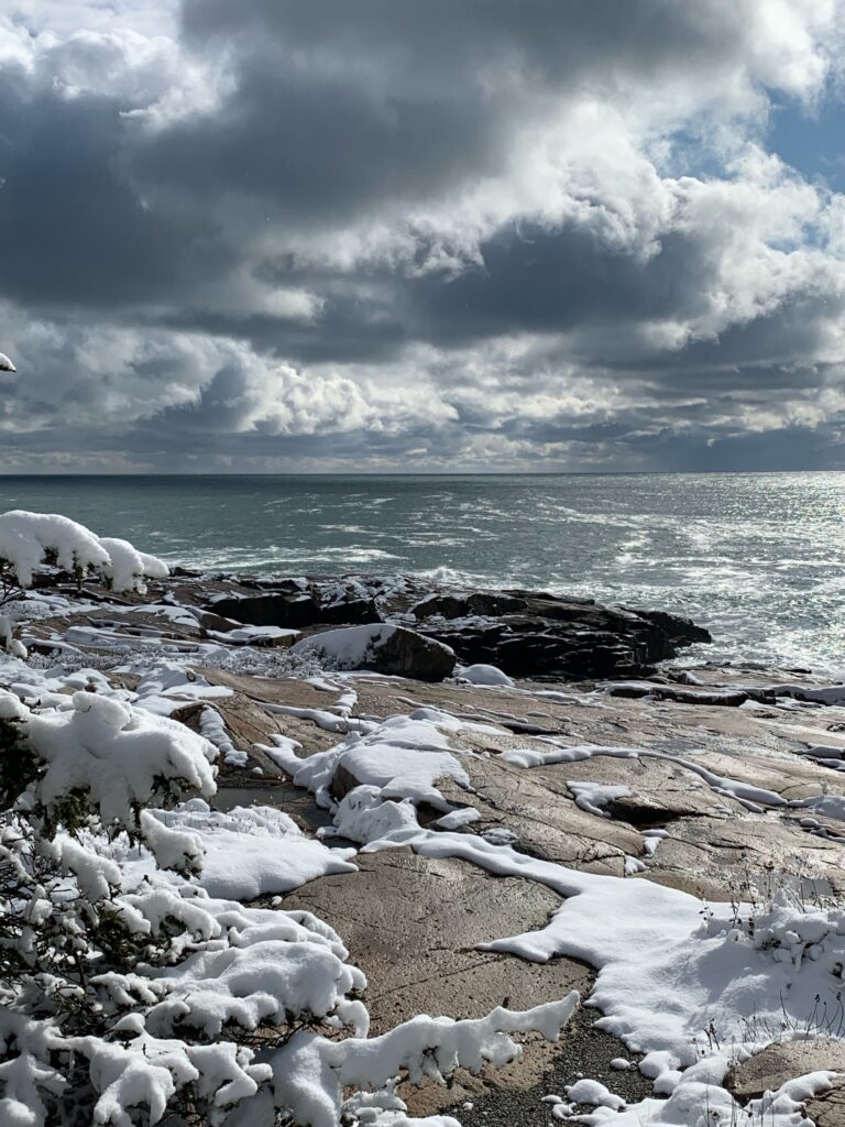 dramatic clouds and sun over the ocean and snow-covered rocks of schoodic point