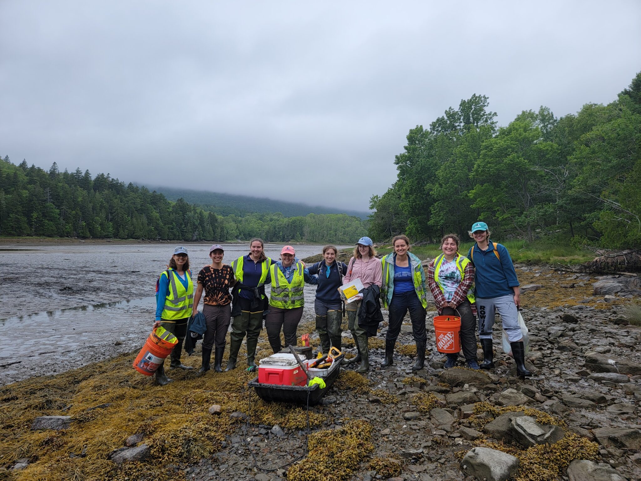 A group of muddy but smiling people pose for a photo in the intertidal zone.