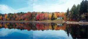 Fall foliage on Little Echo Lake, Mount Desert Island. Blue sky in background and reflected in water in the foreground.