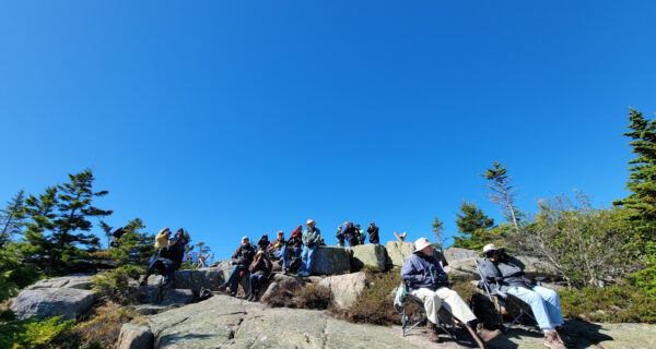 a group of about fifteen people sitting on rocky ledge looking through binoculars