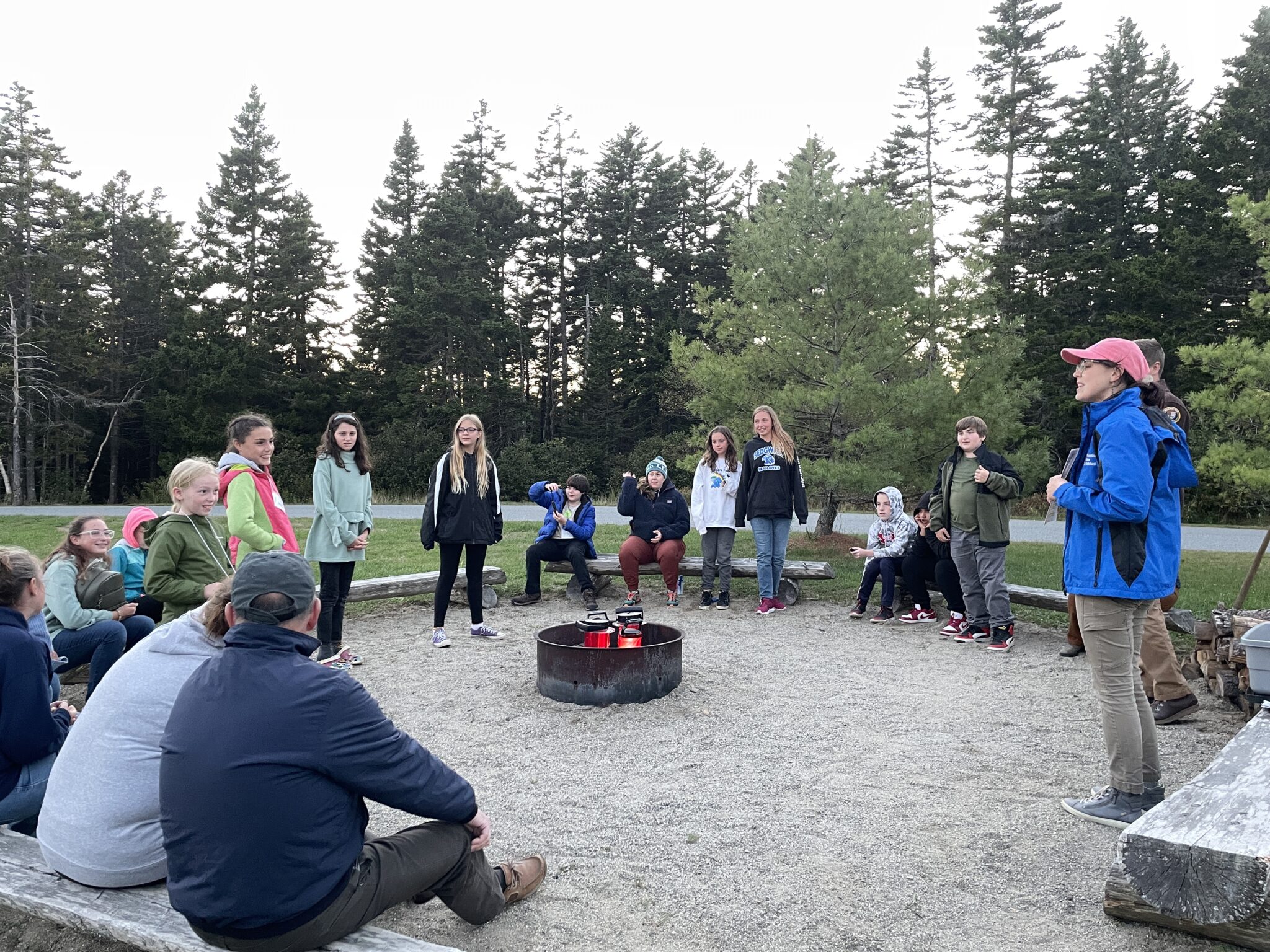 View of middle school students as part of the Schoodic Education Adventure program sitting around a campfire area on the Schoodic Institute campus. 