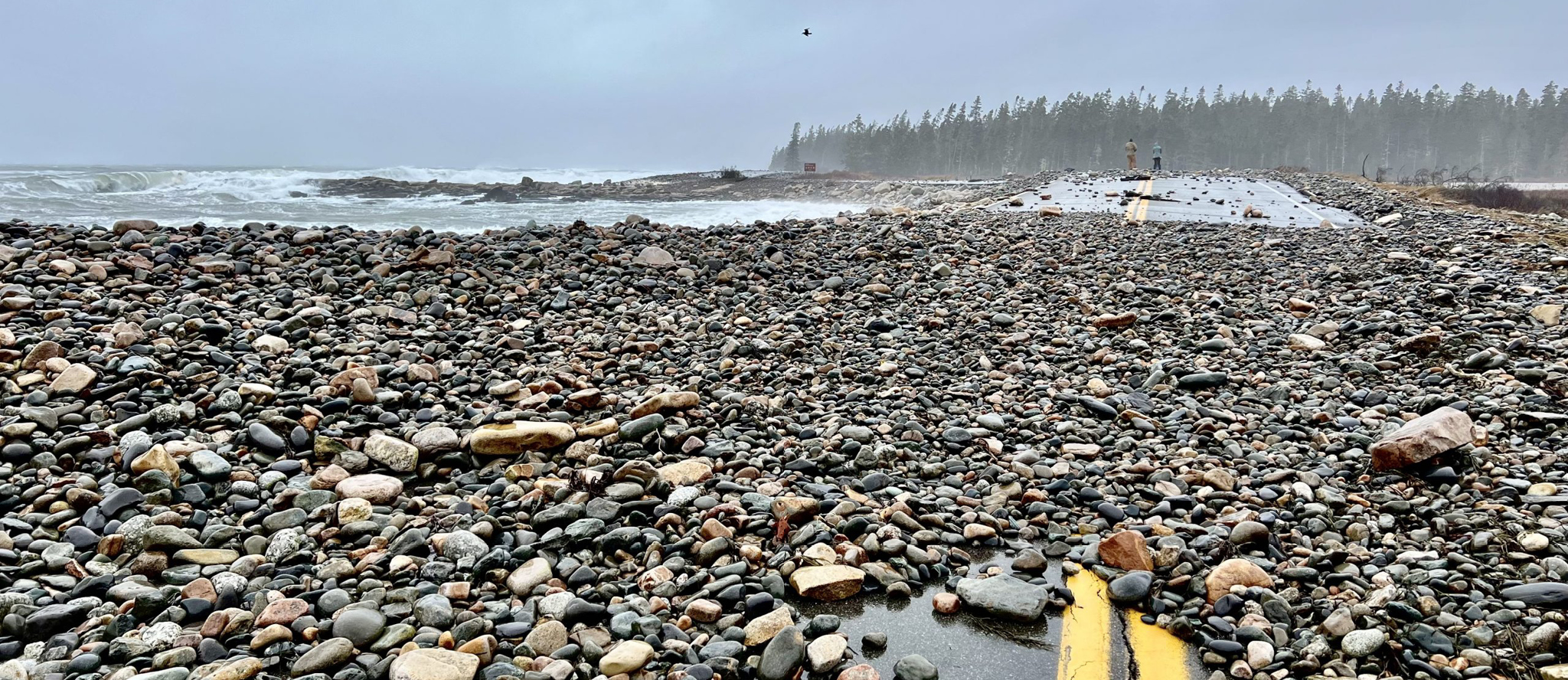 Ocean tide rising as indicated in photo by tide-swept rocks covering a public road.