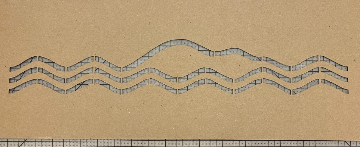 cardboard stencil of three wavy lines. the top line mirrors the profile of Mount Desert Island