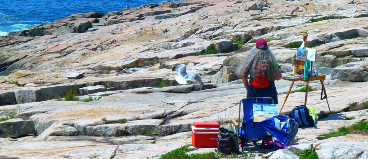 A plein-air painter works on a painting of the Maine coast.