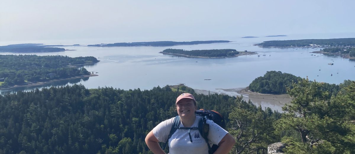 Jamie Attanasio, Schoodic Institute Forest Ecology Technician, stands at the summit of a mountain in Acadia National Park.