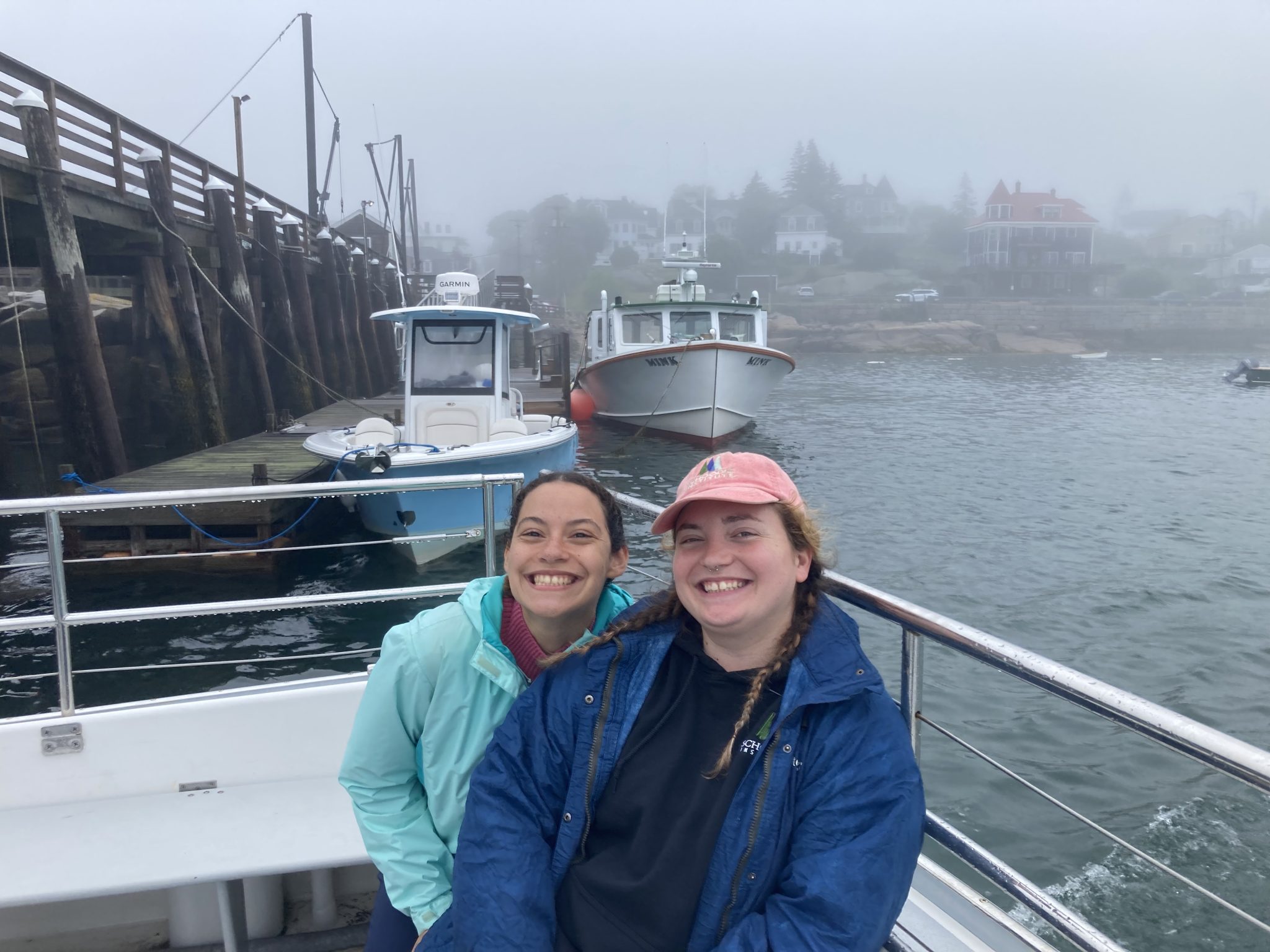 Two members of the forest and monitoring crew for Acadia National Park sit in a boat, smiling at the camera, in Stonington Harbor.