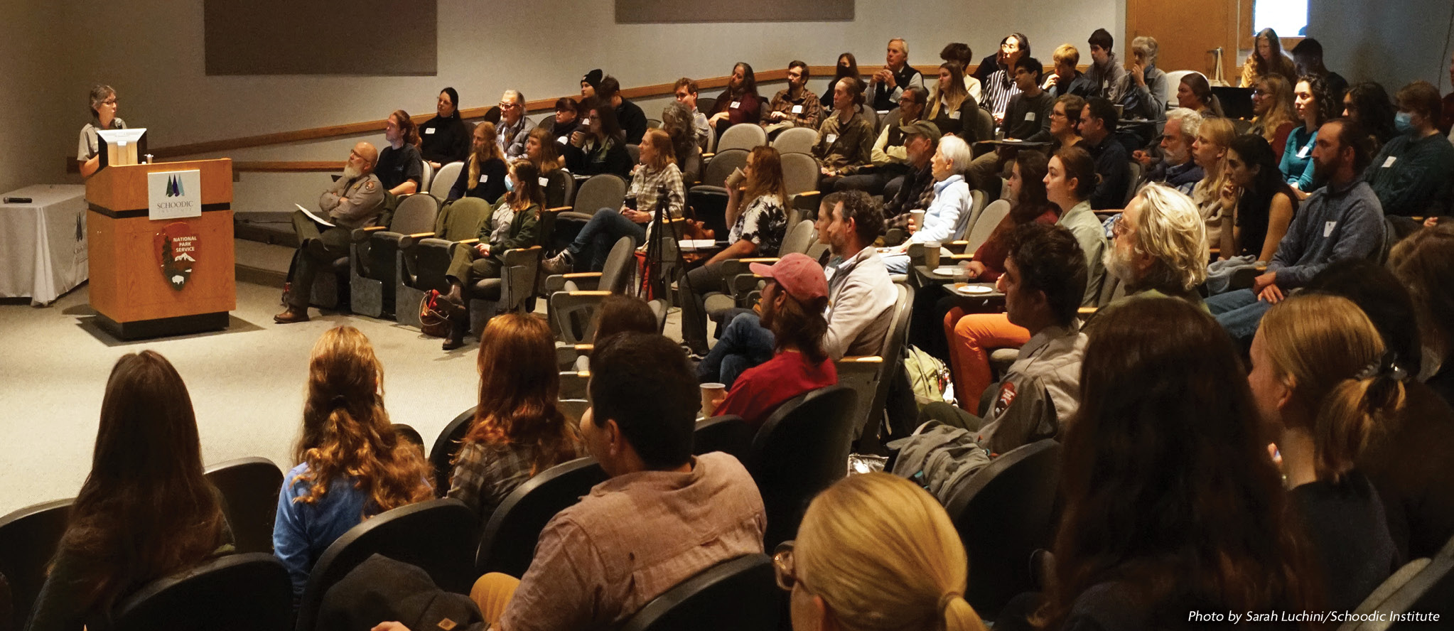 A crowded auditorium at Schoodic Institute listens attentively to a speaker during the Acadia Science Symposium.