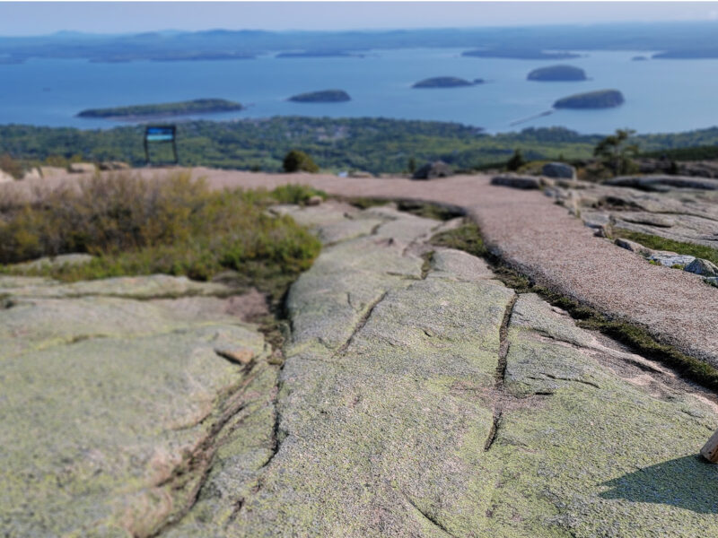 View from the summit of Cadillac Mountain in Acadia National Park on a bright day, looking outward toward the ocean beyond.