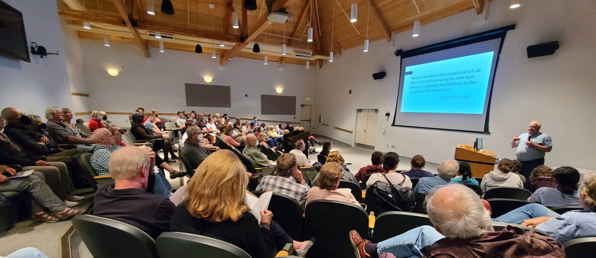 A crowded audience at Moore Auditorium on the Schoodic Institute campus listens to a speaker in the front of the room near a projector screen.
