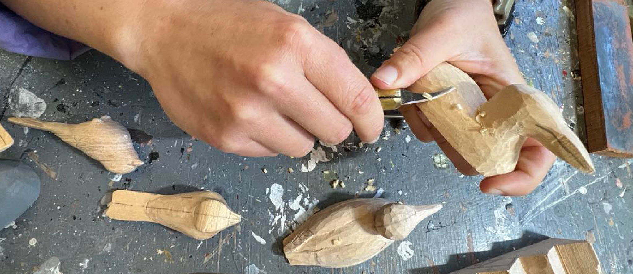 A close-up view of hands carving a block of wood into a bird