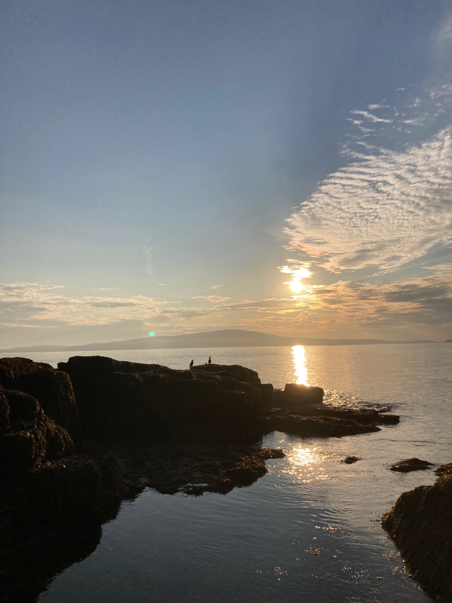 The sun sets on the Schoodic Peninsula coast, casting a warm glow over the water.