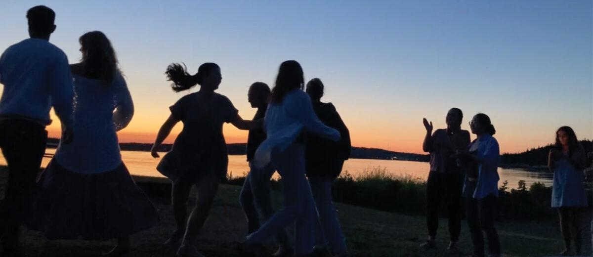 Silhouetted by the setting sun, a group of people joyfully dance near the ocean.