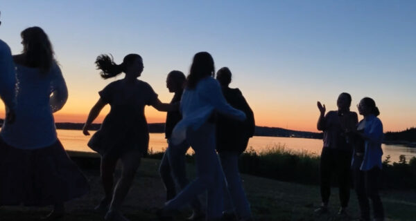 Silhouetted by the setting sun, a group of people joyfully dance near the ocean.