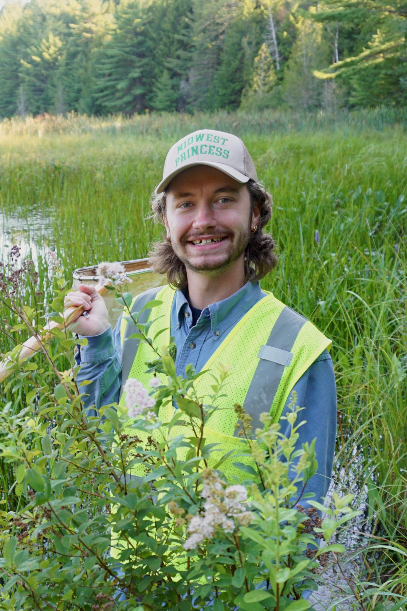 Trevor Grandin stands in a meadow among tall grasses while smiling at the camera