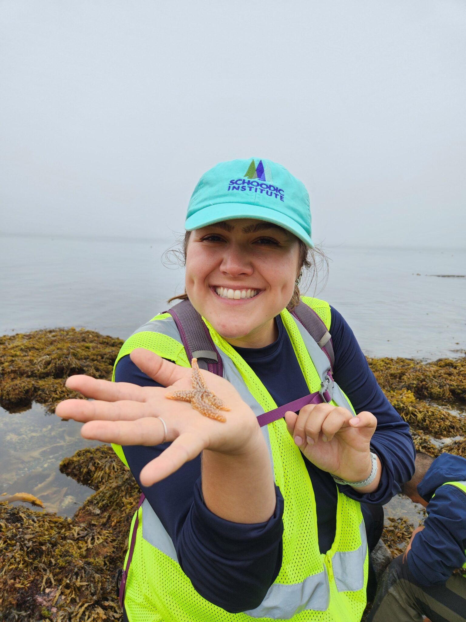 With the foggy ocean horizon behind her, Stephanie Letourneau excitedly holds up a sea star to the camera