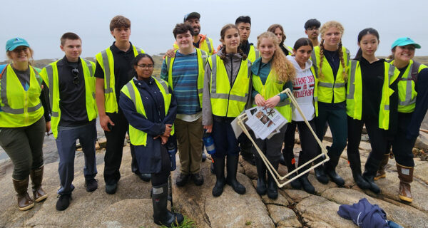 A group of young students gather together for a photo along the coastline of the Schoodic Peninsula on a foggy day