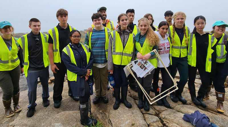 A group of young students gather together for a photo along the coastline of the Schoodic Peninsula on a foggy day