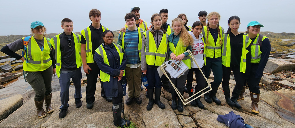 A group of young students gather together for a photo along the coastline of the Schoodic Peninsula on a foggy day