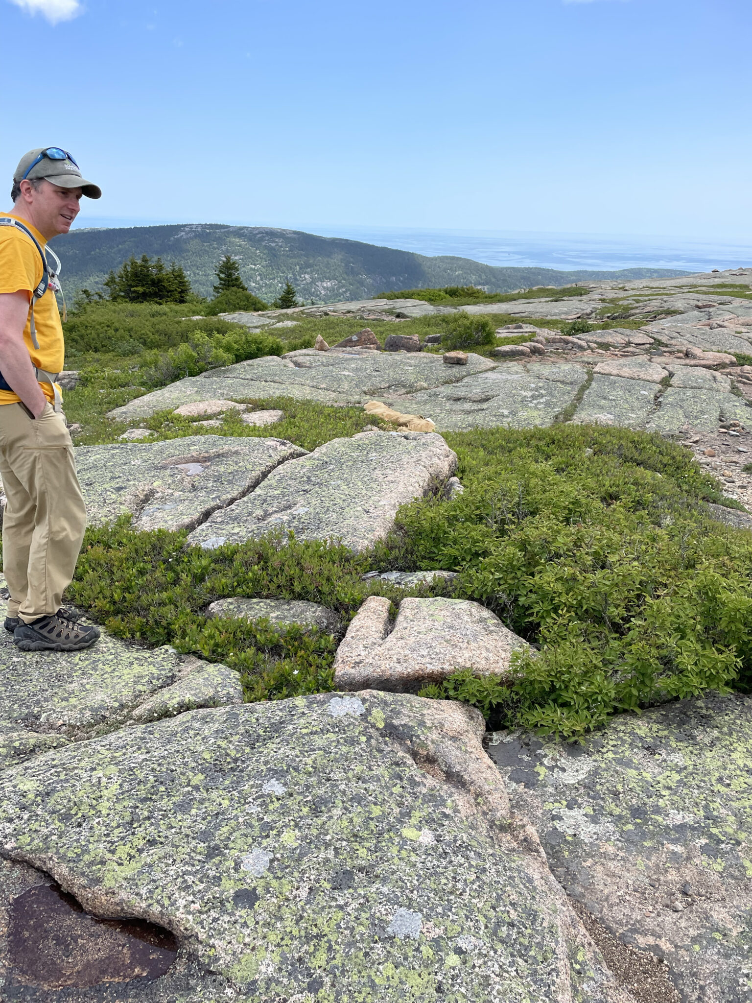 Under a clear blue sky, Chris Nadeau hikes towards a mountain summit in Acadia National Park 