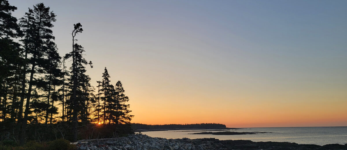 The sun rises over the Schoodic Peninsula coast, casting warm light over the horizon