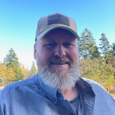 Jim McLean smiles at the camera in front of trees and a blue sky
