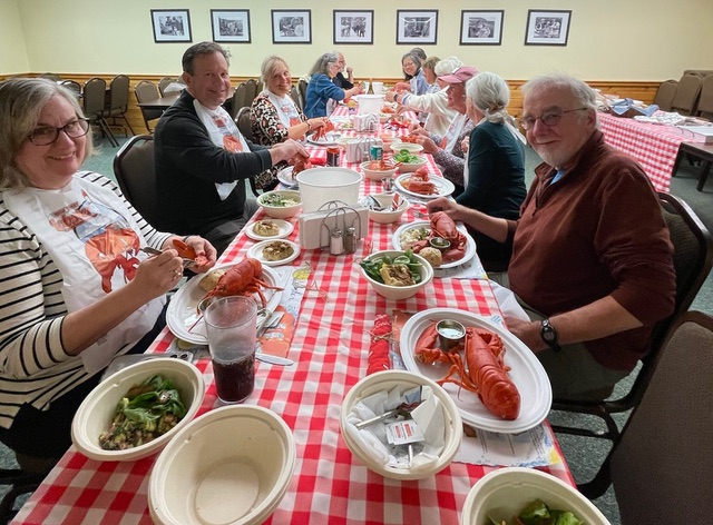Participants in a painting workshop gather around a restaurant table with a red and white checkered tablecloth while enjoying a lobster dinner 
