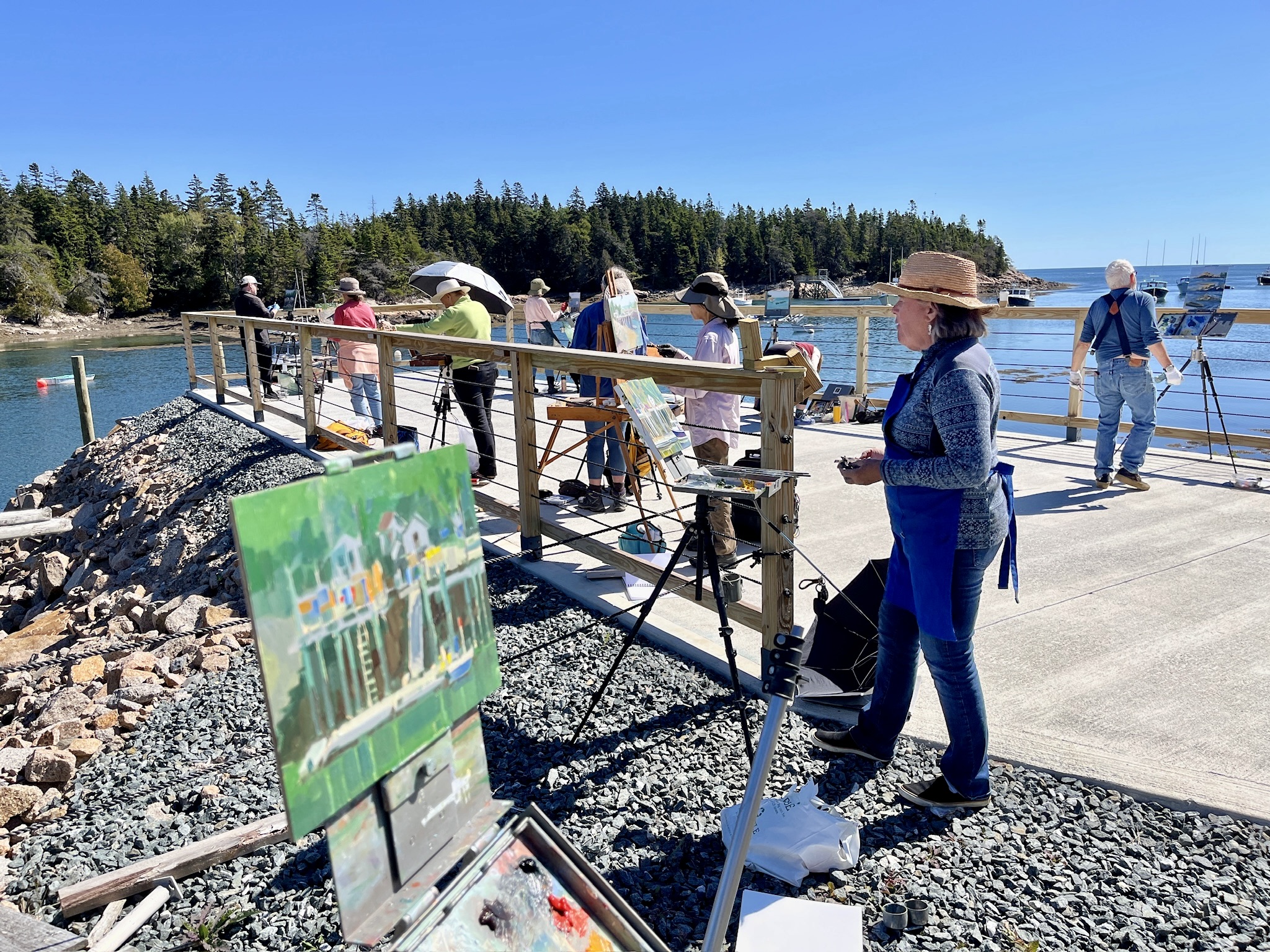 A group of painters gather along the coast while painting at their easels
