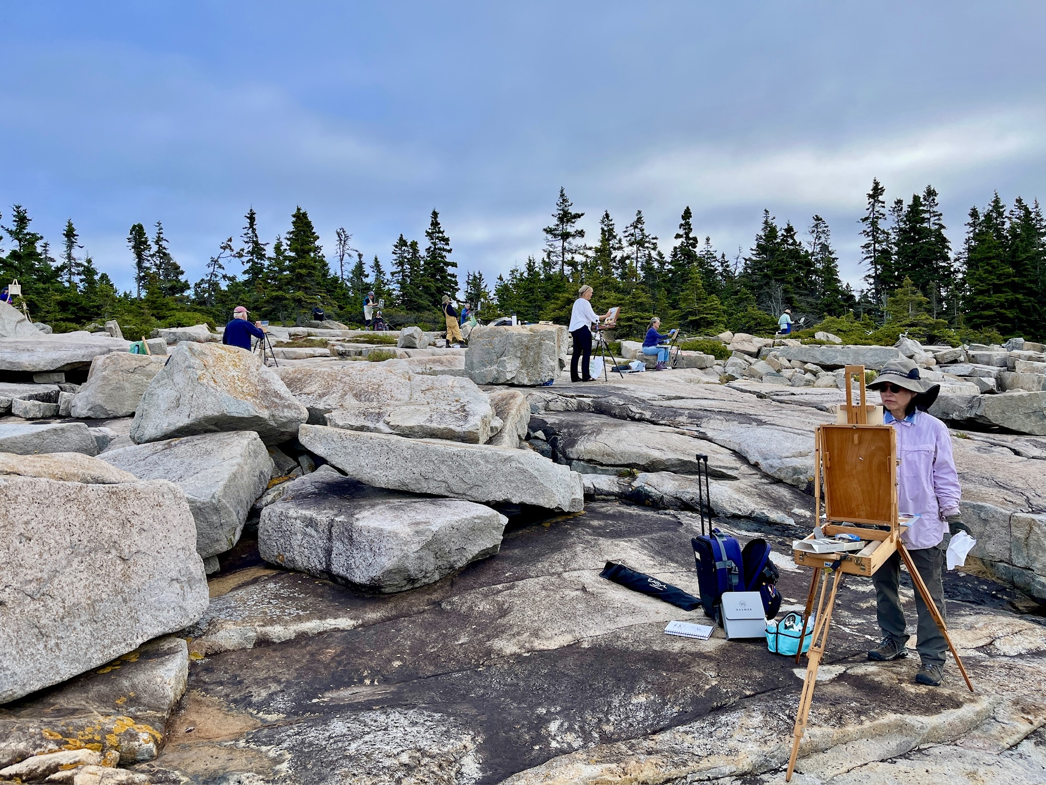 A group of painters gather along the rocks near Schoodic Point while painting at their easels 