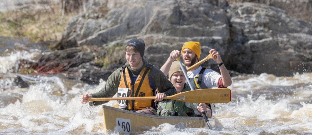 three people paddle a canoe through rapids