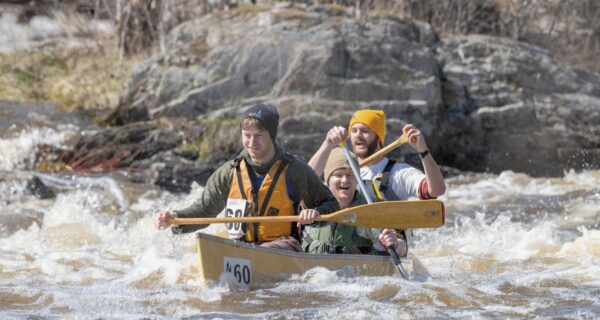 three people paddle a canoe through rapids