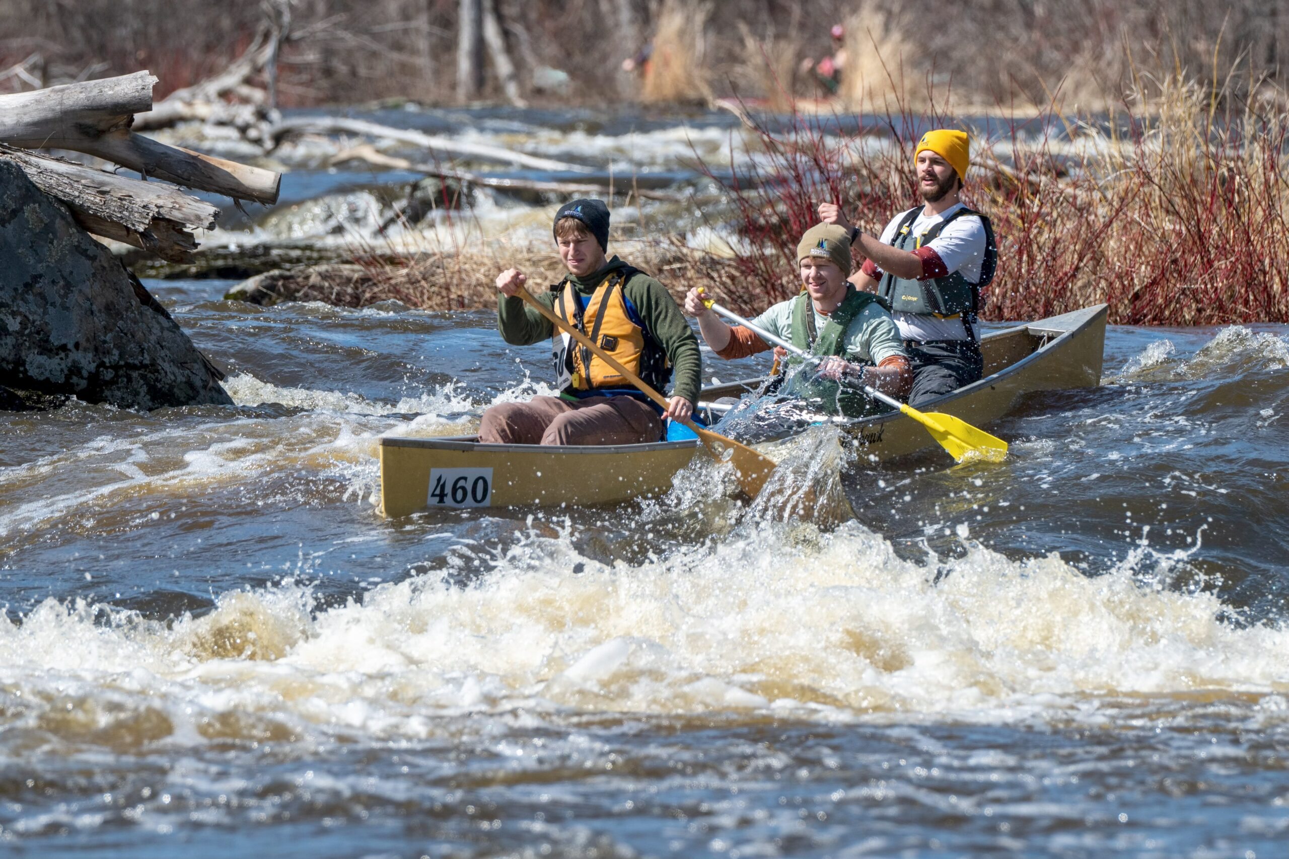 three people paddle a canoe through whitewater rapids